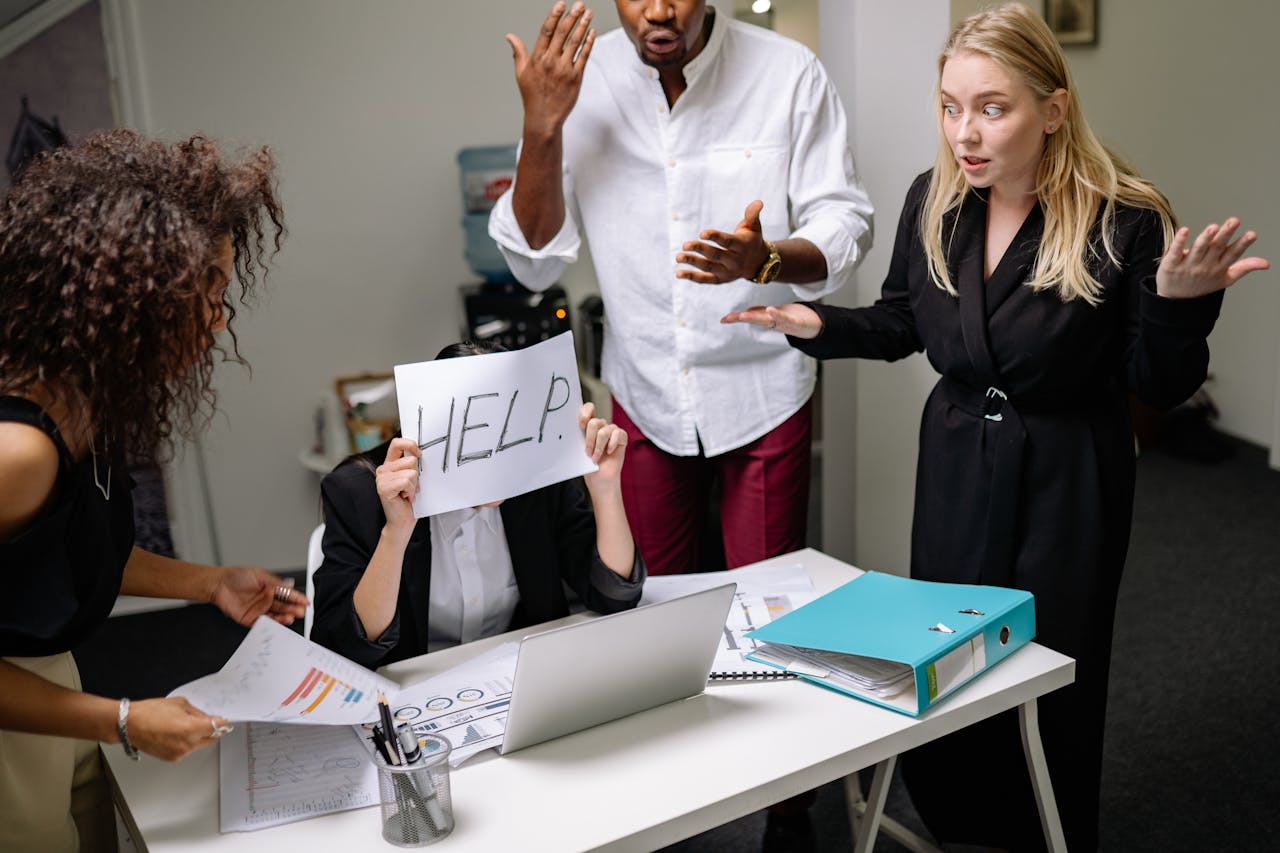 home-services-01 A group of employees in heated discussion, one holding a HELP sign, indicates workplace stress.